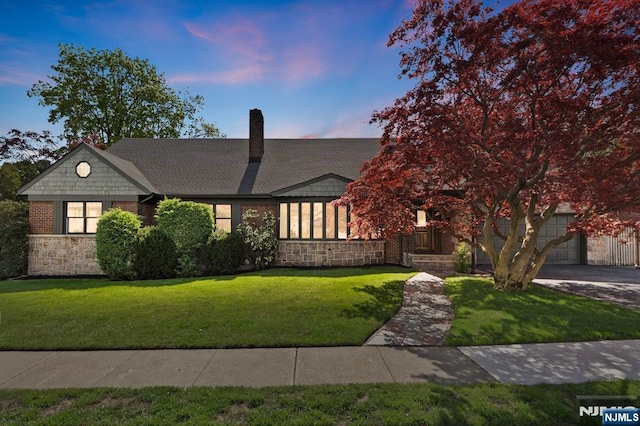tudor house featuring stone siding, an attached garage, a front lawn, and driveway