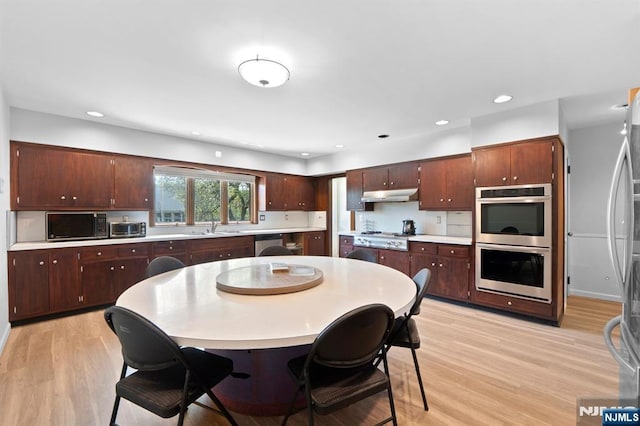kitchen with under cabinet range hood, stainless steel appliances, light countertops, a sink, and light wood-style flooring