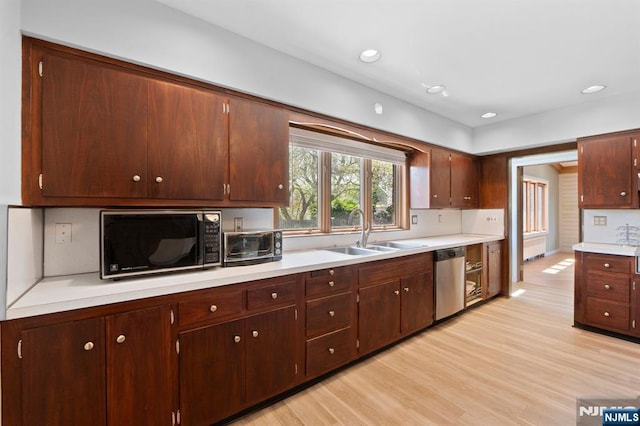 kitchen featuring stainless steel dishwasher, a sink, black microwave, light wood finished floors, and light countertops