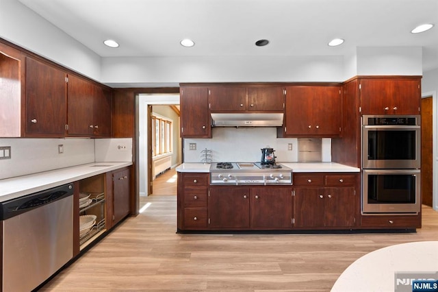 kitchen with stainless steel appliances, light wood-style flooring, under cabinet range hood, and light countertops