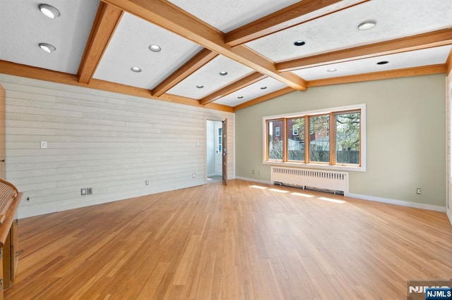 unfurnished living room with radiator heating unit, wooden walls, baseboards, and light wood-style floors