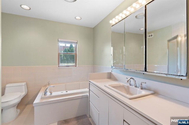 bathroom featuring a garden tub, vanity, tile walls, toilet, and recessed lighting