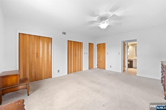 unfurnished bedroom with visible vents, connected bathroom, carpet floors, two closets, and ceiling fan