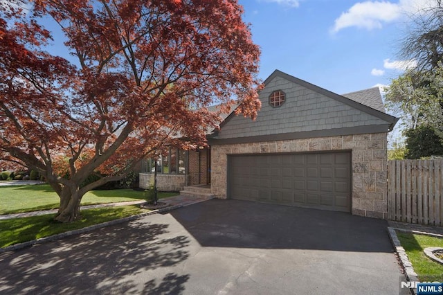 view of property hidden behind natural elements with driveway, fence, stone siding, and a garage