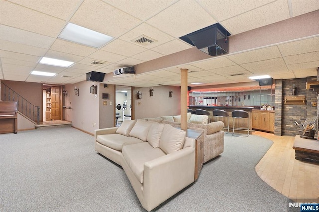 living room featuring visible vents, stairs, a drop ceiling, and indoor bar