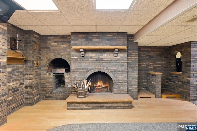 unfurnished living room with brick wall, an outdoor brick fireplace, hardwood / wood-style floors, and a drop ceiling