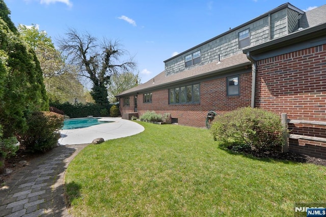 exterior space with brick siding, a yard, roof with shingles, and an outdoor pool