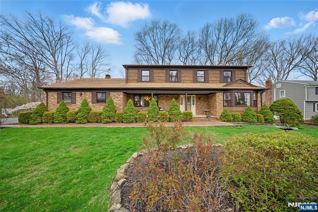 traditional-style home featuring a chimney, covered porch, a front yard, and brick siding