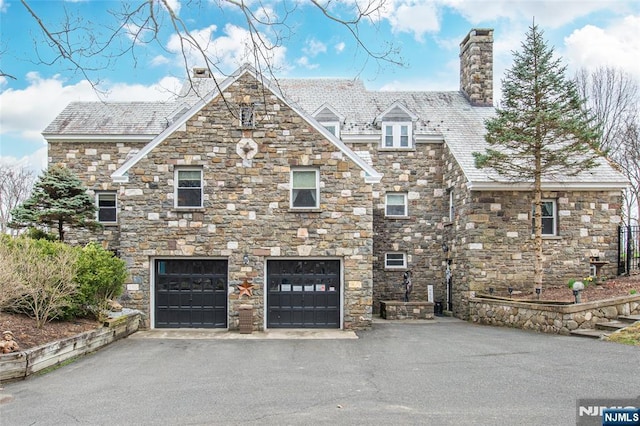 view of front of property featuring a chimney, an attached garage, driveway, and stone siding