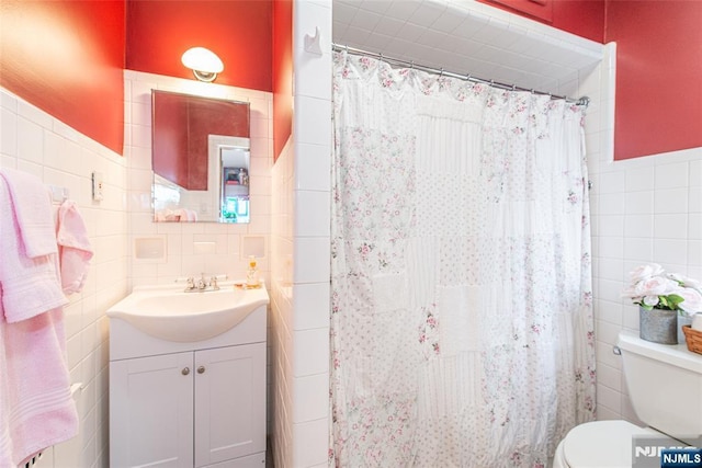 bathroom with a wainscoted wall, toilet, vanity, tile walls, and a shower with shower curtain