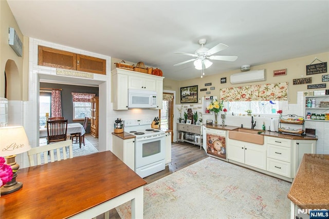 kitchen featuring white cabinets, a ceiling fan, a wall unit AC, a sink, and white appliances