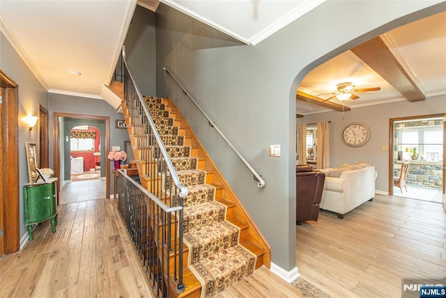 stairway featuring wood finished floors, a ceiling fan, ornamental molding, arched walkways, and baseboards