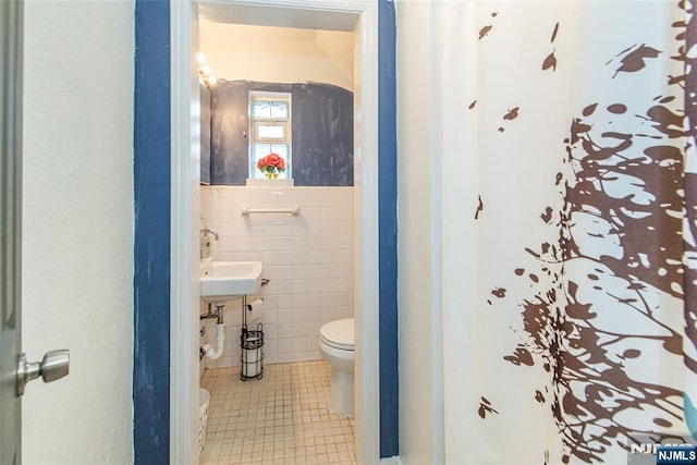 half bathroom with tile walls, toilet, a sink, and tile patterned floors