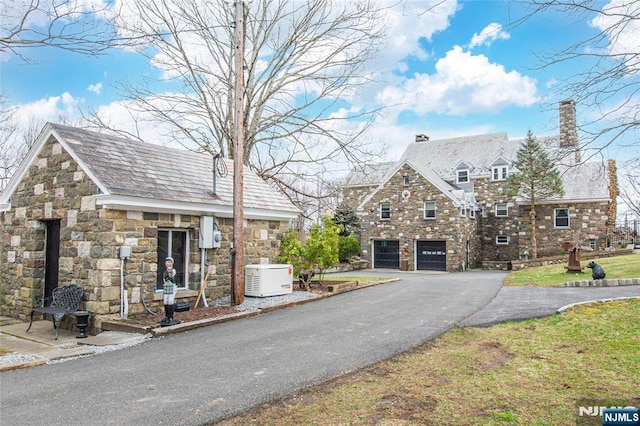 view of front of house featuring a chimney, aphalt driveway, stone siding, and a garage