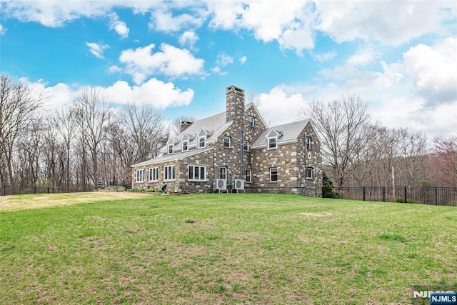rear view of house with a lawn, a chimney, fence, and stone siding