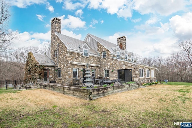 rear view of property with stone siding, a chimney, and a yard