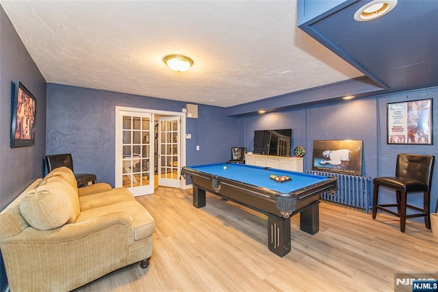 game room with wood finished floors, pool table, a textured wall, and french doors
