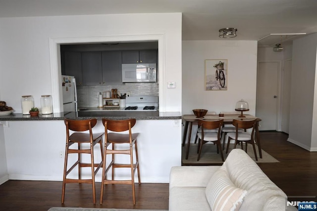 25 River Unit B10, Nutley, NJ 07110 - kitchen with a breakfast bar, dark countertops, white appliances, tasteful backsplash, and dark wood-style flooring