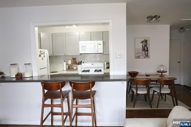 25 River Unit B10, Nutley, NJ 07110 - kitchen with backsplash, white appliances, a peninsula, a breakfast bar area, and dark wood-style flooring