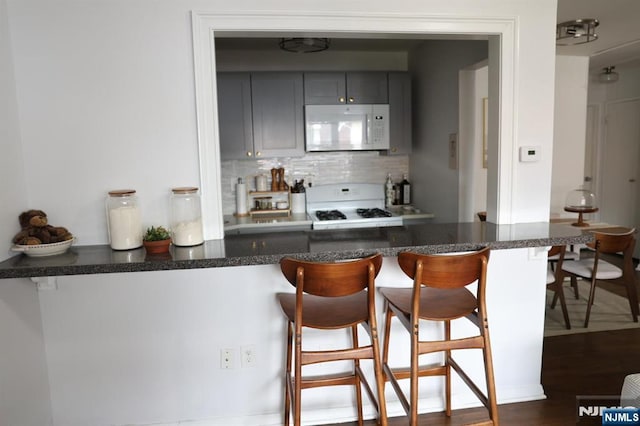 25 River Unit B10, Nutley, NJ 07110 - kitchen featuring dark wood-style floors, gray cabinets, white appliances, a kitchen bar, and tasteful backsplash