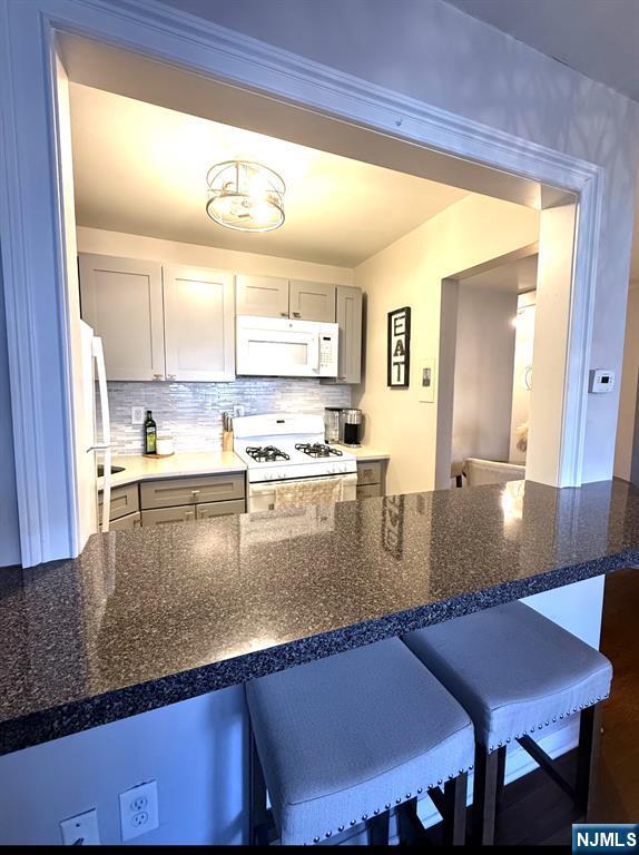 25 River Unit B10, Nutley, NJ 07110 - kitchen featuring a breakfast bar, tasteful backsplash, gray cabinetry, and white appliances