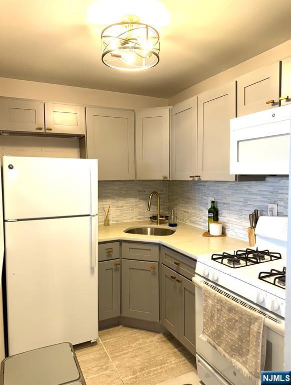 25 River Unit B10, Nutley, NJ 07110 - kitchen featuring a sink, white appliances, gray cabinets, light countertops, and backsplash