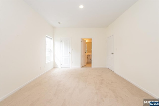 unfurnished bedroom with recessed lighting, ensuite bathroom, light colored carpet, and baseboards