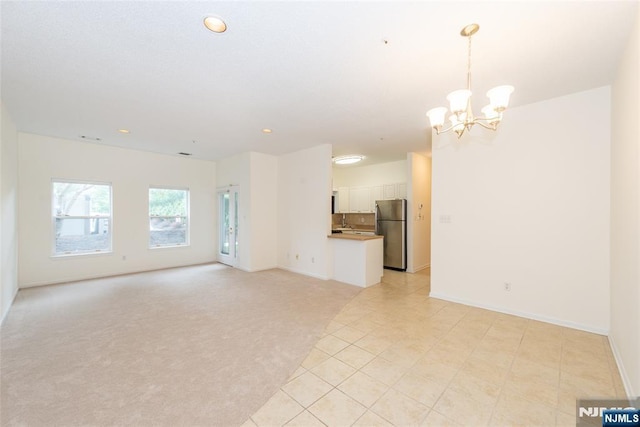 unfurnished living room with light tile patterned floors, light colored carpet, a chandelier, and baseboards