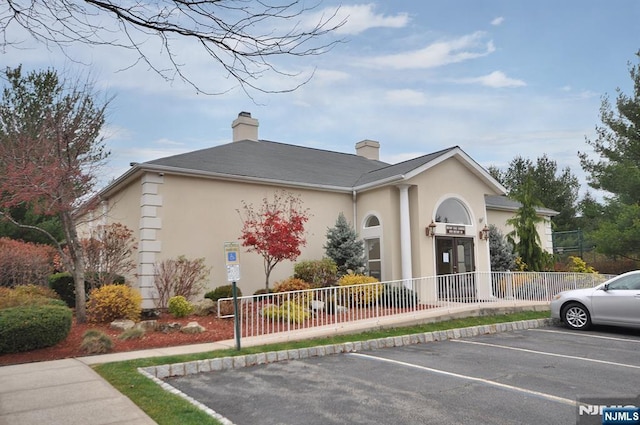 view of front of property with uncovered parking, stucco siding, fence, and a chimney