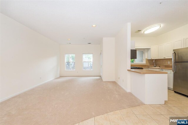 kitchen featuring freestanding refrigerator, a peninsula, white cabinets, light carpet, and a sink