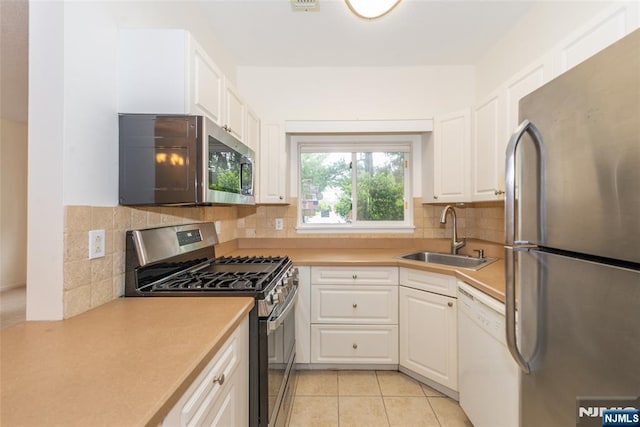 kitchen with white cabinets, a sink, light countertops, stainless steel appliances, and light tile patterned flooring