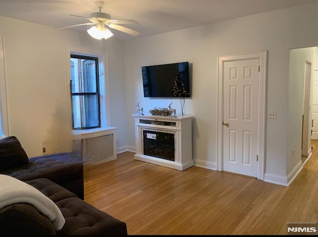 living room with ceiling fan, baseboards, a glass covered fireplace, and light wood-style floors