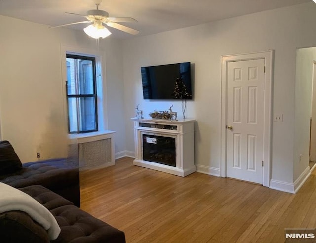 living area featuring a glass covered fireplace, light wood-type flooring, baseboards, and ceiling fan