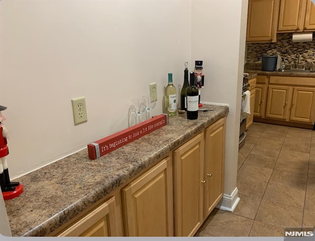 kitchen with a sink, dark countertops, backsplash, range, and light tile patterned floors