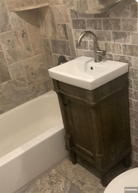 bathroom featuring tile walls, toilet, vanity, and a bathing tub