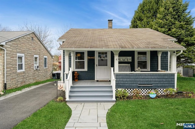 bungalow-style home featuring a porch, a shingled roof, a front lawn, and a chimney