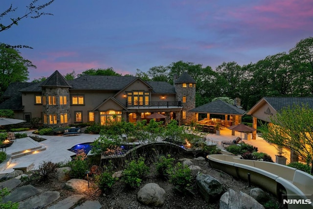 22 Nottingham Ct, Ringwood, NJ 07456 - back of property at dusk featuring a balcony, a patio, an outdoor fire pit, stucco siding, and an outdoor pool