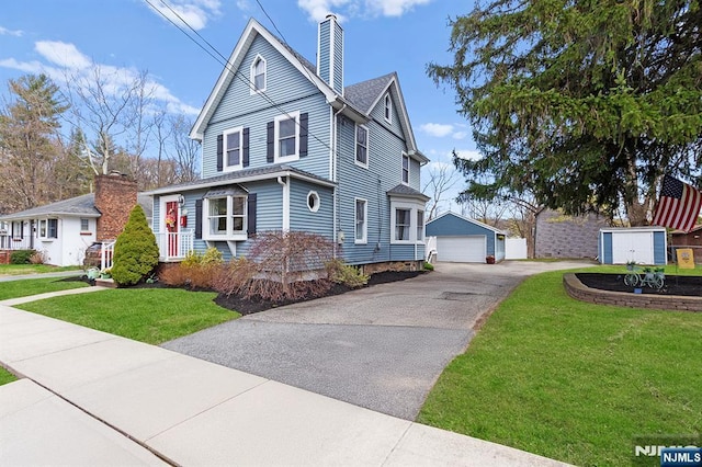 victorian home with an outdoor structure, a chimney, a front yard, and a garage