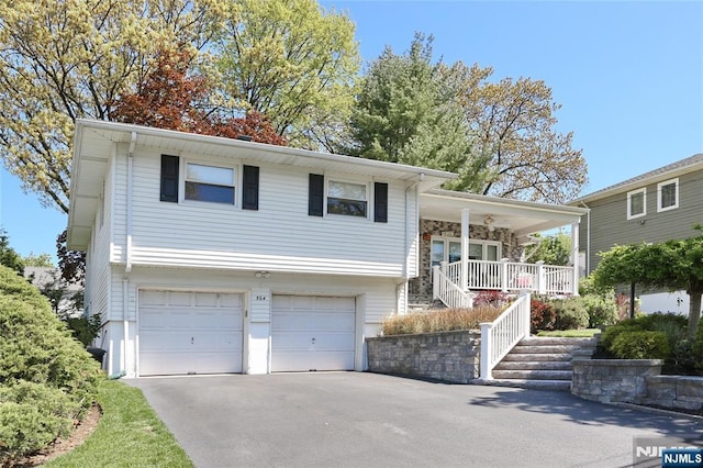 tri-level home with a porch, a garage, and aphalt driveway