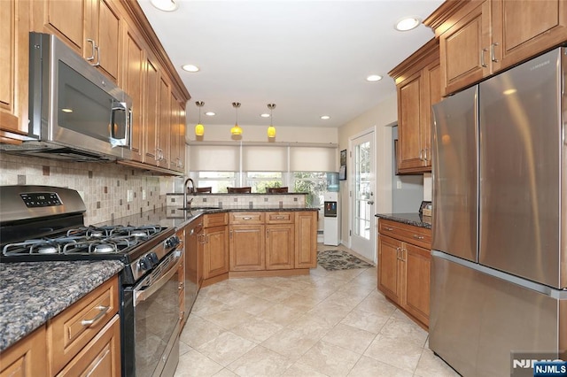 kitchen featuring appliances with stainless steel finishes, tasteful backsplash, brown cabinets, a sink, and a peninsula