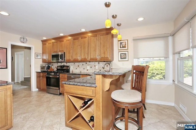 kitchen featuring visible vents, a peninsula, a kitchen bar, dark stone counters, and appliances with stainless steel finishes