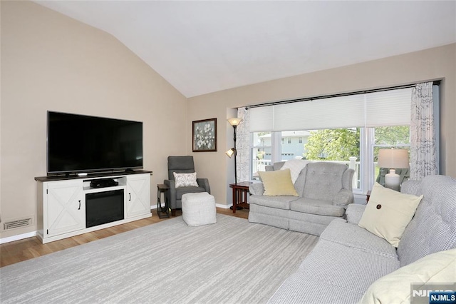 living area with plenty of natural light, vaulted ceiling, wood finished floors, and visible vents