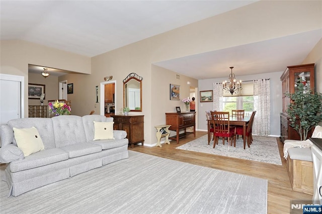 living area featuring baseboards, a notable chandelier, lofted ceiling, and light wood-style floors
