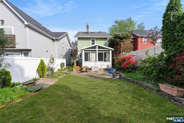 rear view of property with a fenced backyard, a yard, a chimney, and a sunroom