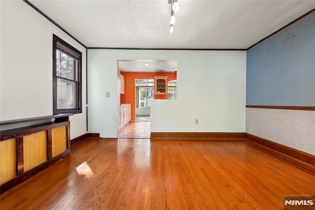 unfurnished living room with light wood-style floors, ornamental molding, baseboards, and wallpapered walls