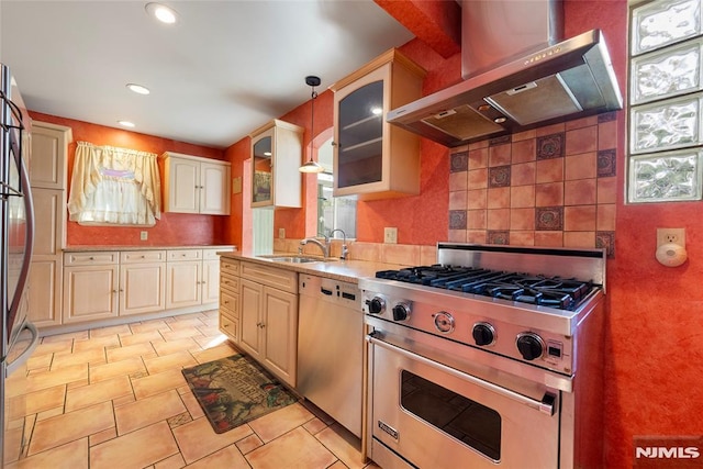 kitchen featuring appliances with stainless steel finishes, a sink, light countertops, wall chimney exhaust hood, and glass insert cabinets