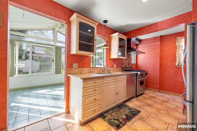 kitchen featuring glass insert cabinets, wall chimney range hood, light countertops, a sink, and stainless steel appliances