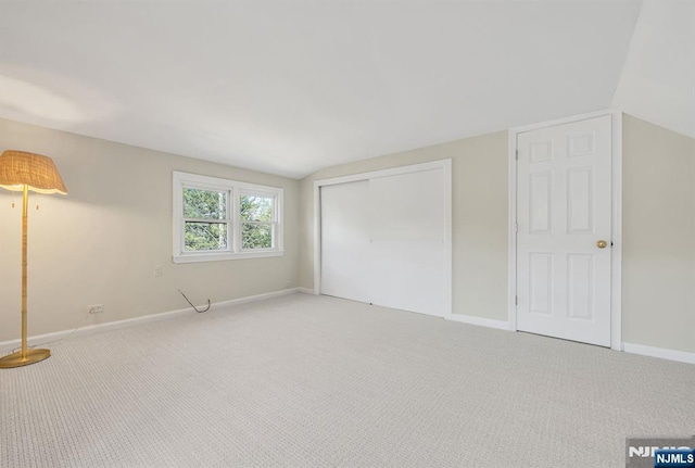unfurnished bedroom with lofted ceiling, a closet, baseboards, and light carpet