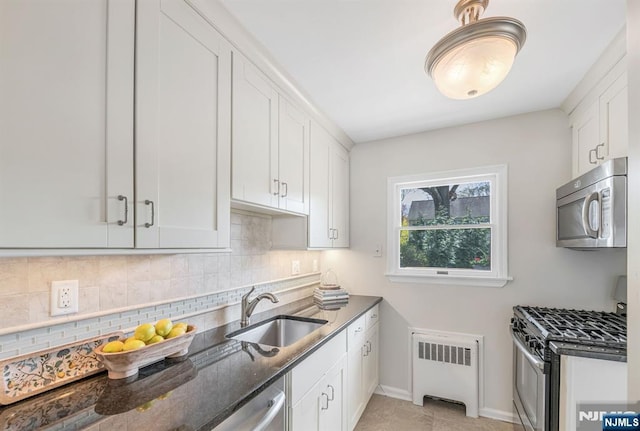 kitchen with stainless steel appliances, a sink, dark stone countertops, tasteful backsplash, and radiator