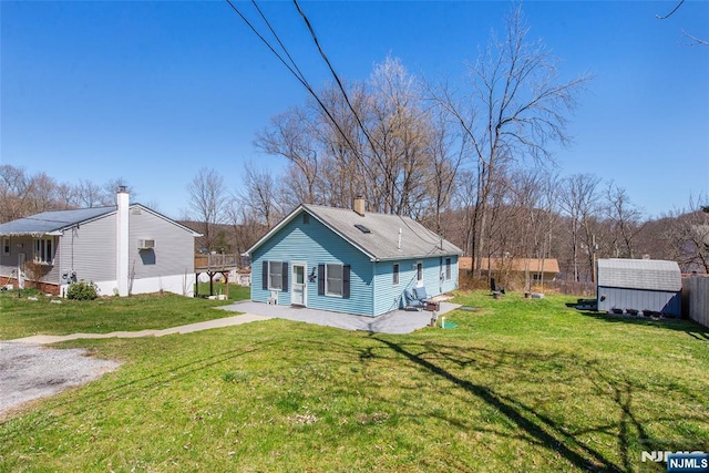 back of property with an outdoor structure, a yard, a shed, and a chimney